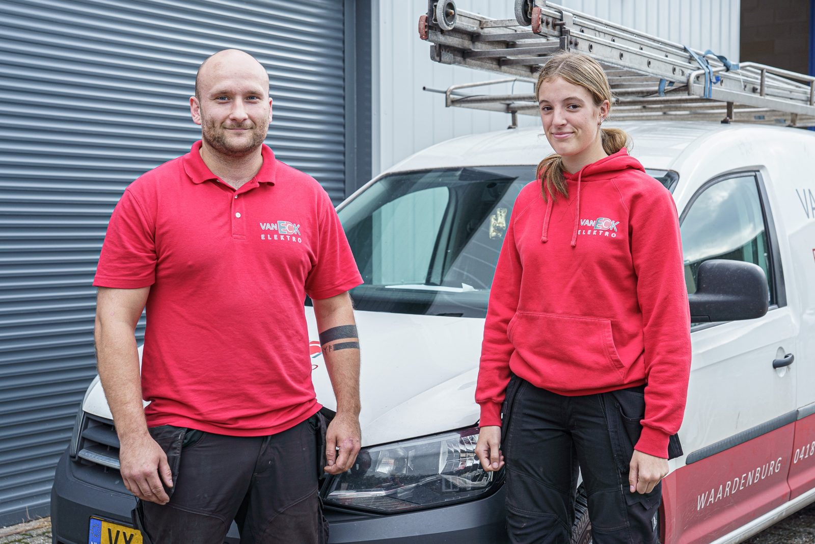 Elektrotechnisch monteur Remik en leerling-monteur Nynke bij een bedrijfsbus van Van Eck Elektro