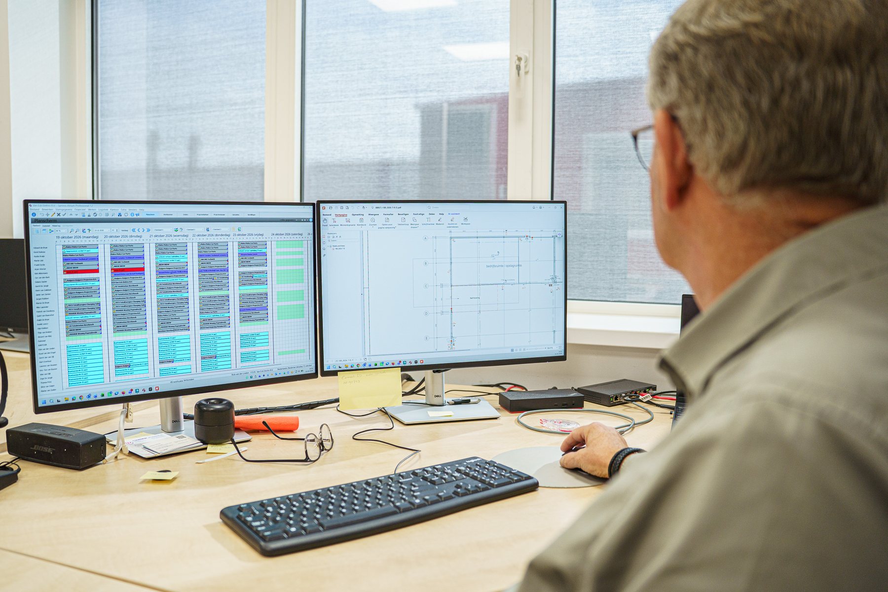 Een collega van Van Eck maakt de planning op kantoor, met de bouwtekening op het tweede scherm
